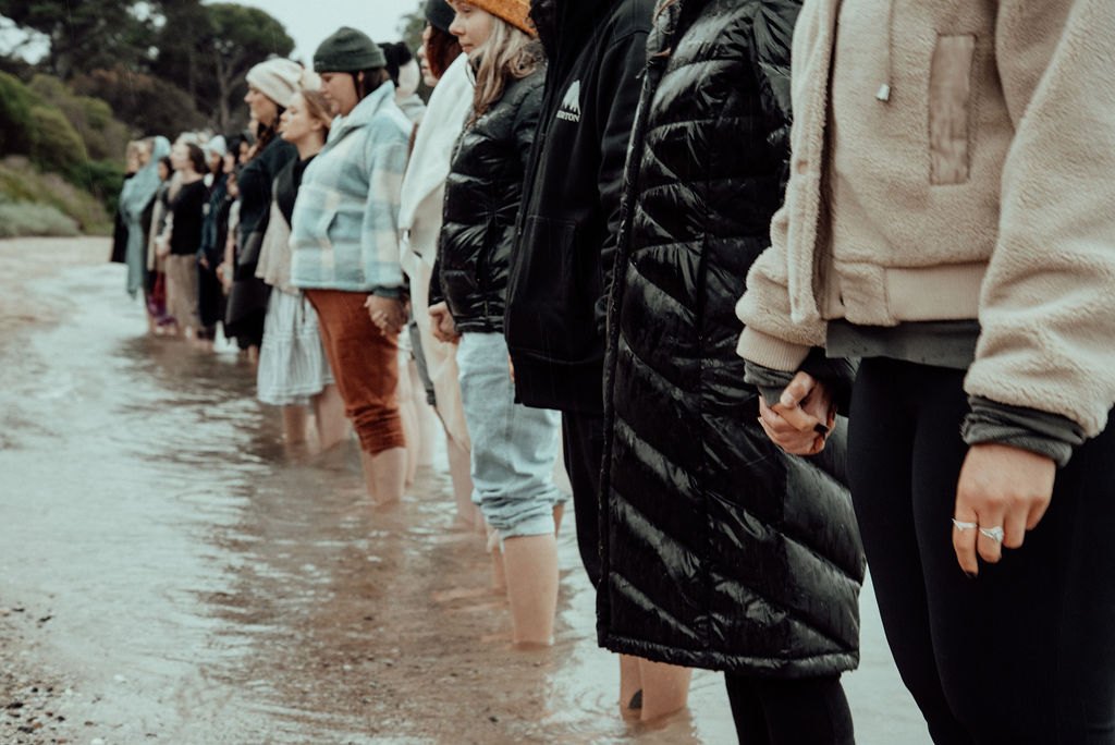 Women standing together hand in hand at the shoreline